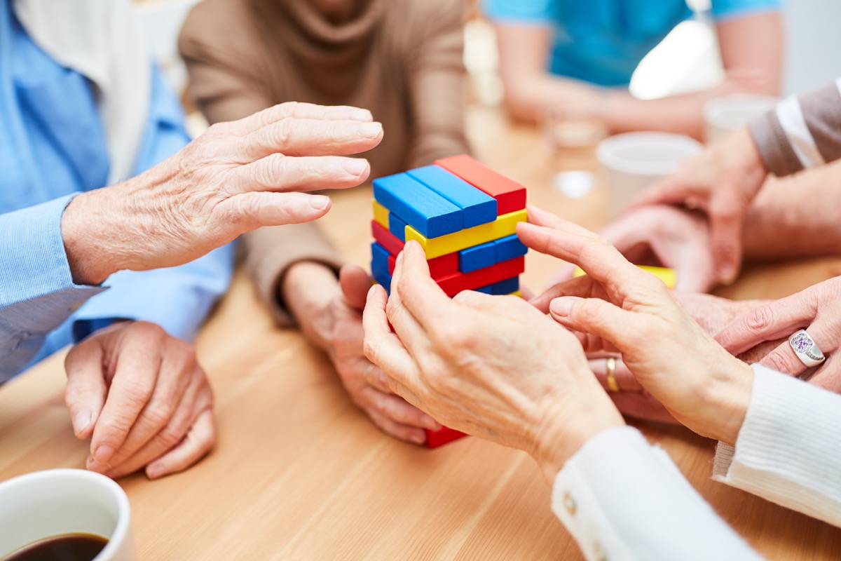 Group seniors with dementia builds a tower in the nursing home from colorful building blocks